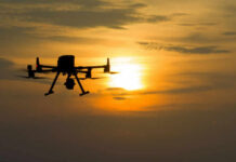 A silhouette of a drone flying against a sunset sky
