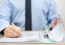 Mayor’s ‘Engagement’ Office Sparks Outrage A person in a blue shirt writing on a document while holding a binder