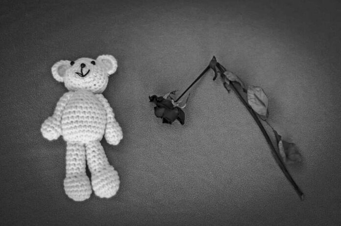 A crocheted teddy bear next to a wilted rose on a textured surface