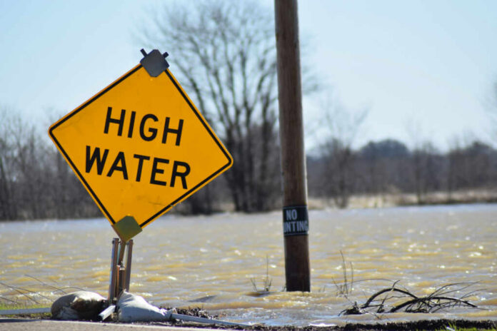 shutterstock_1326218726 A high water warning sign near a flooded area