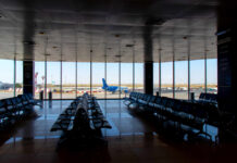 Airport departure lounge with empty seating facing large windows
