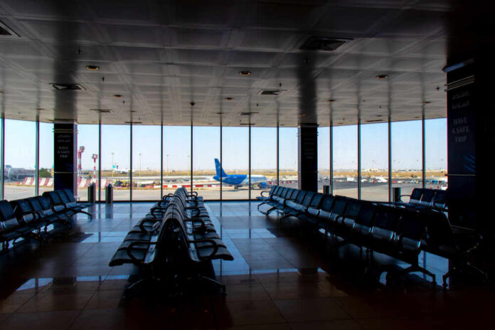 Airport departure lounge with empty seating facing large windows