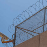 Security camera mounted on a barbed wire fence against a clear blue sky