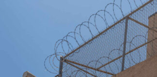 Security camera mounted on a barbed wire fence against a clear blue sky