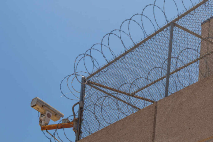 Security camera mounted on a barbed wire fence against a clear blue sky
