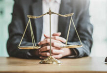 10,000 Government Lawyers Gone—Good Or Bad? A lawyers hands resting on a table with a scale of justice in front
