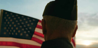 Wounded Vets Helped—By High Schoolers A veteran in uniform standing in front of an American flag during sunset