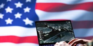 Military Prepares For GPS Failure Laptop with surveillance software against a blurred American flag