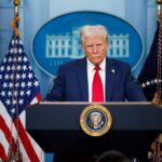 A political figure at a podium during a press conference in front of the White House
