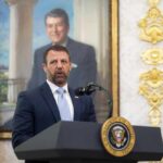 Man in a suit speaks at a presidential podium
