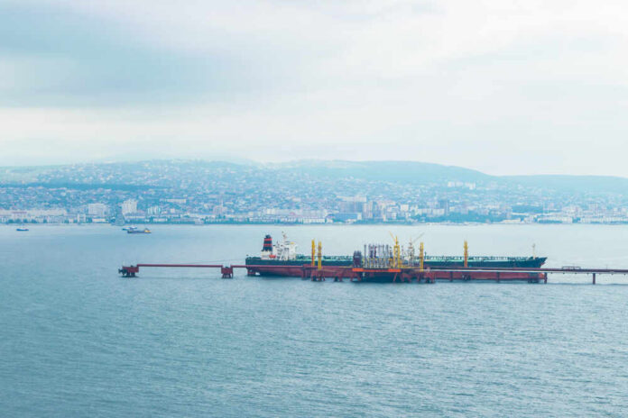 Oil tanker docked at a shipping port with a coastal city in the background