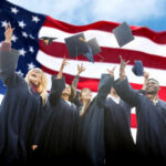 Group of graduates joyfully throwing their caps in front of an American flag