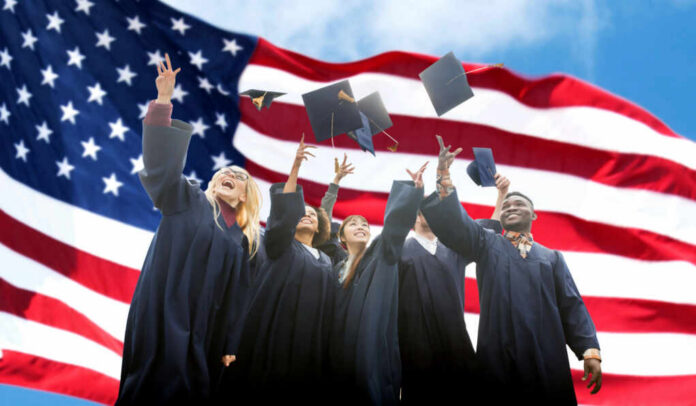 shutterstock_568420213 Group of graduates joyfully throwing their caps in front of an American flag