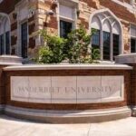 Historic brick university building with central tower framed by green trees