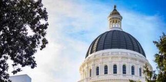View of a state capitol dome with American and California flags against a blue sky
