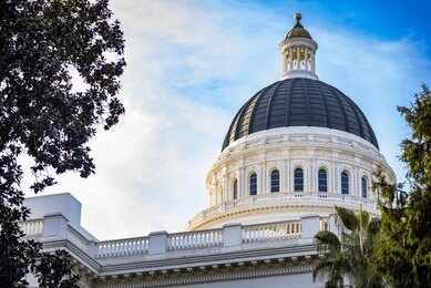 2743106471 View of a state capitol dome with American and California flags against a blue sky