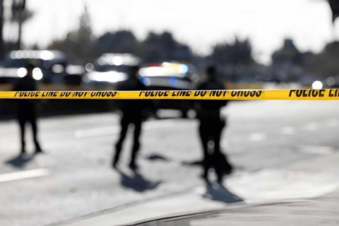 Police tape cordons off a street with blurred officers and vehicles in the background