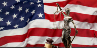 Defamation Gambit Targets Capitol Hero A gavel and a statue of Lady Justice in front of an American flag