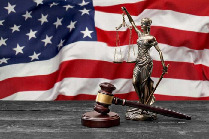 shutterstock2356835469jpg A gavel and a statue of Lady Justice in front of an American flag