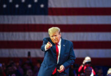 Bridges Next: Trump’s Chilling Iran Ultimatum A speaker in a suit gesturing towards the audience in front of an American flag