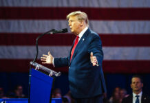 Trump Warns Of Communist Threat A man in a suit speaking at a podium with an American flag in the background