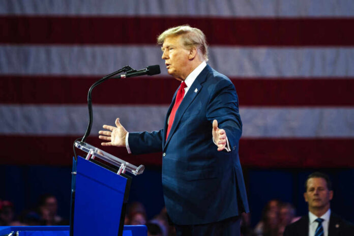 shutterstock2455398299jpg A man in a suit speaking at a podium with an American flag in the background
