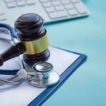 Gavel and stethoscope on medical clipboard near keyboard