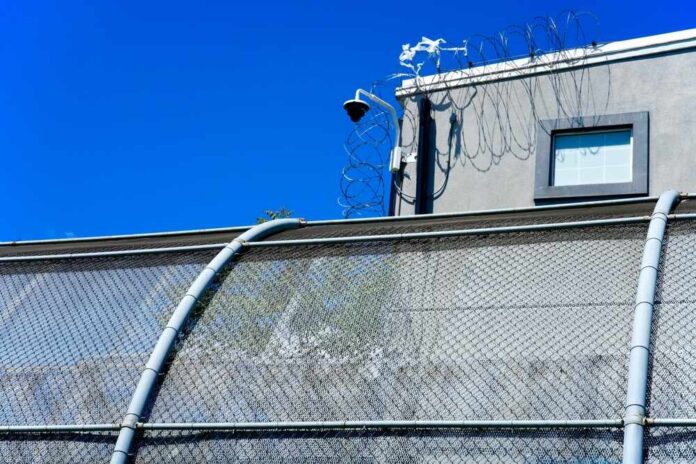 Newark,,Nj,,Usa,-,May,10,,2025:,Delaney,Hall,Is Security camera mounted above a prison fence with barbed wire against a blue sky