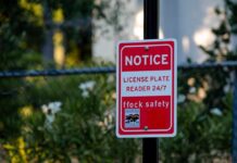 Red notice sign on a black pole in a leafy outdoor area