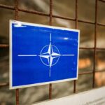 NATO emblem on a blue sign attached to a rusty wire fence