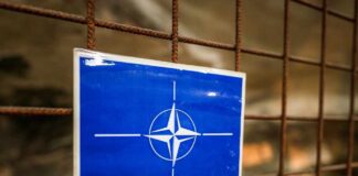 France Boosts NATO’s Northern Force NATO emblem on a blue sign attached to a rusty wire fence