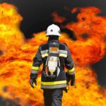 Firefighter in protective gear facing large flames