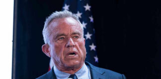 RFK Jr. Blasts CNN — ‘Press Malpractice’ Man holding microphone, speaking with American flag behind.