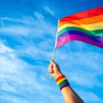 Hand holding a rainbow pride flag against a blue sky
