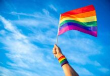 Questions Follow Talarico Pride Festival Role Hand holding a rainbow pride flag against a blue sky