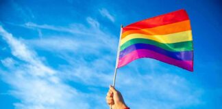 Questions Follow Talarico Pride Festival Role Hand holding a rainbow pride flag against a blue sky