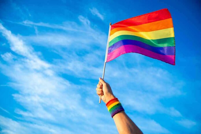 Hand holding a rainbow pride flag against a blue sky