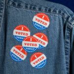 denim jacket with multiple red white and blue voting stickers