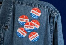 denim jacket with multiple red white and blue voting stickers