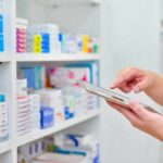 Pharmacist using a tablet in front of stocked pharmacy shelves
