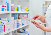 Pharmacist using a tablet in front of stocked pharmacy shelves