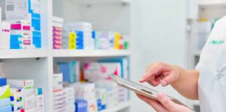 Pharmacist using a tablet in front of stocked pharmacy shelves
