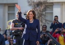 Power Grab? Harris Targets Supreme Court woman in navy suit waving at an outdoor event