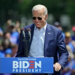 Man in sunglasses speaking at outdoor rally podium