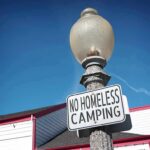 Street lamp with a no camping sign against a blue sky