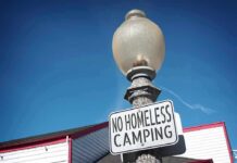 Outrage Brews: Sleeping Outside Now A Crime? Street lamp with a no camping sign against a blue sky