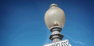 Outrage Brews: Sleeping Outside Now A Crime? Street lamp with a no camping sign against a blue sky