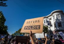Democrat Denies Backing Police Defunding protesters holding signs at a street demonstration
