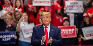 man in suit clapping at indoor rally