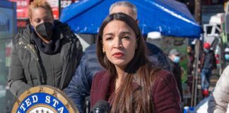 Defund Flip? AOC Laughs, Voters Bristle Woman speaking at outdoor press event with microphones and seal